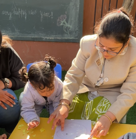A teacher and a toddler enjoying a craft activity together at the school table