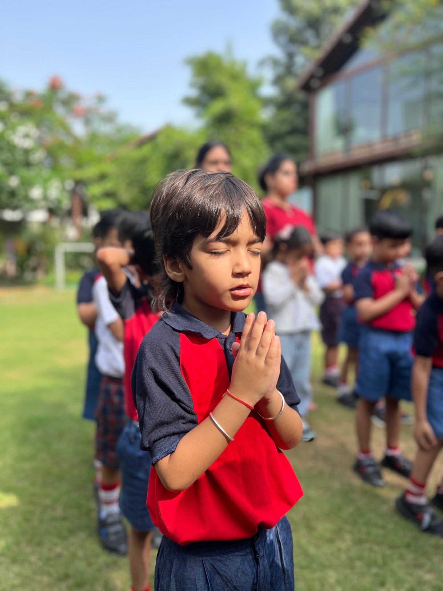 A girl standing with folded hands during the morning prayer on the lawn