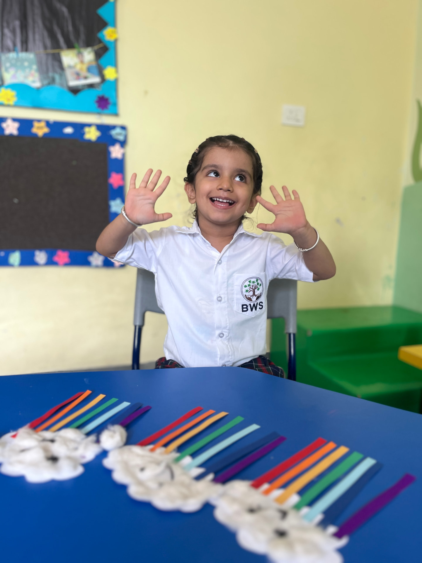 A preschooler waving both hands at her craft table in class